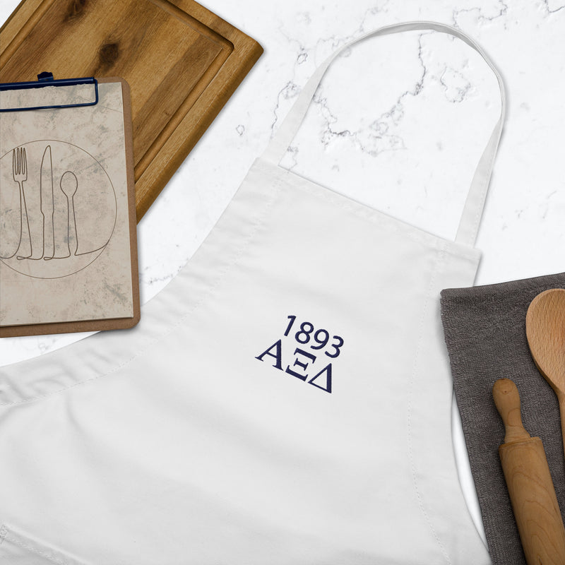 Alpha Xi Delta Embroidered Apron in white with Navy blue letters shown in kitchen setting