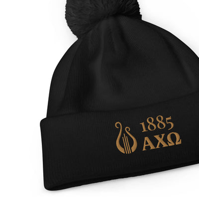 Alpha Chi Omega 1885 Lyre Pom Pom Beanie shown in black with gold embroidery in close up view