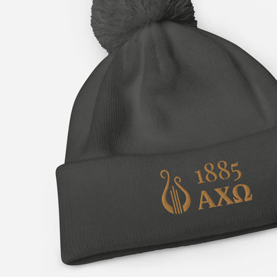Alpha Chi Omega 1885 Lyre Pom Pom Beanie shown in gray with gold embroidery in close up view
