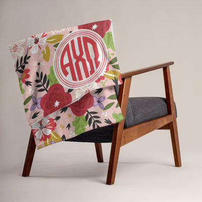 Our Alpha Chi Omega floral print throw blanket in Hera Pink shown over a chair.