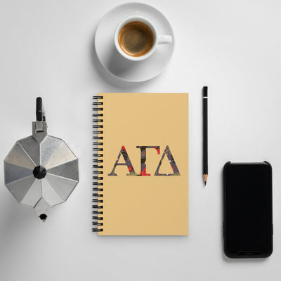 Alpha Gamma Delta Greek Letters Spiral Notebook shown with coffee