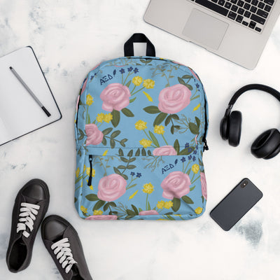 Alpha Xi Delta pink rose floral print backpack blue background shown in lifestyle setting.