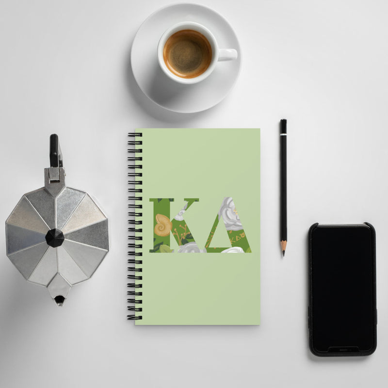 Kappa Delta Greek Letters Spiral Notebook shown with coffee