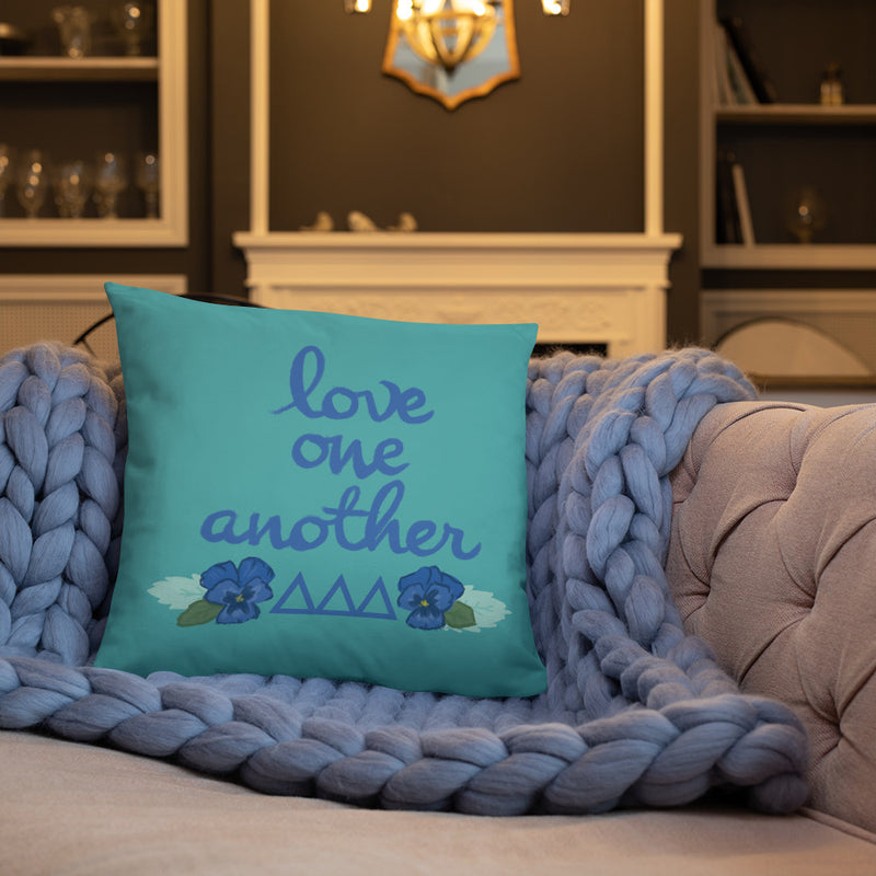 Tri Delta Love One Another Pillow shown on a couch