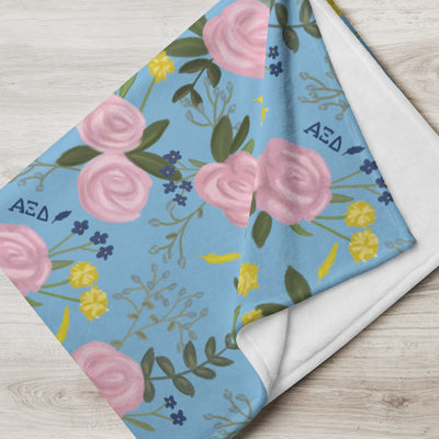 Alpha Xi Delta Pink Rose Throw Blanket shown folded in blue showing white reverse side