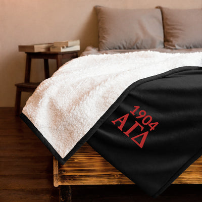 Alpha Gamma Delta Plush Embroidered Sherpa Blanket in black on bed