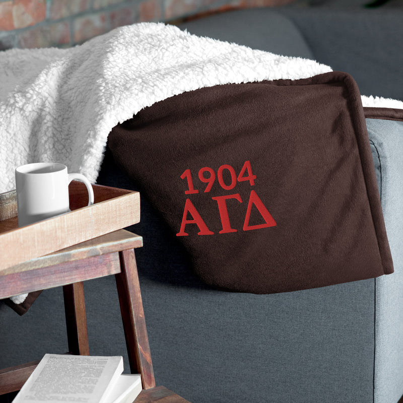 Alpha Gamma Delta Plush Embroidered Sherpa Blanket in brown on couch