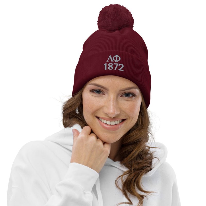 Alpha Phi 1872 Pom-Pom Beanie in burgundy shown on model with letters embroidered in silver