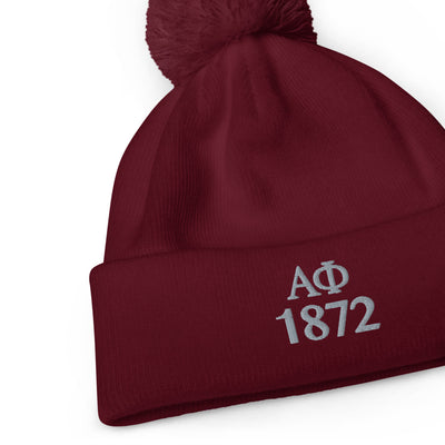 Alpha Phi 1872 Pom-Pom Beanie in burgundy shown flat with letters embroidered in silver