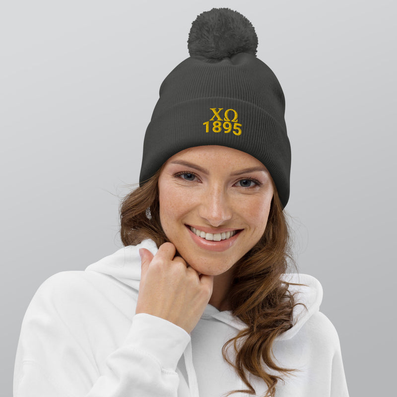 Chi Omega Pom Pom Beanie in gray with gold embroidery shown on model