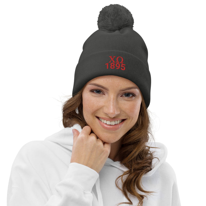 Chi Omega Sorority Pom Pom Beanie in with red embroidery on model in graphite gray