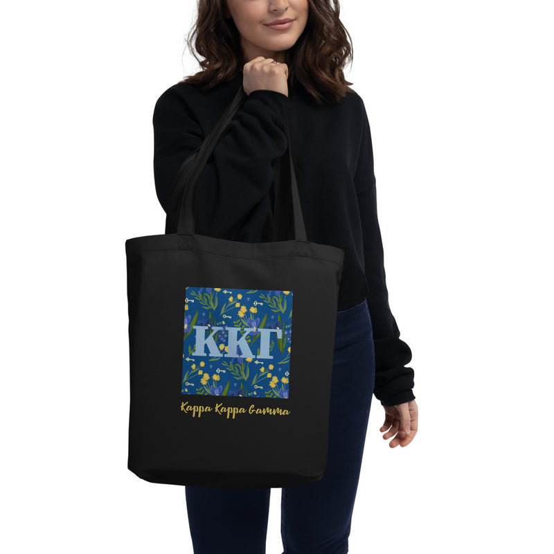 Kappa Kappa Gamma Greek Letters with a blue iris pattern behind. Printed on a black canvas shopping tote.