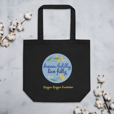 Kappa Kappa Gamma Dream Boldly. Live Fully. motto printed on a black canvas bag shown with cotton blossoms