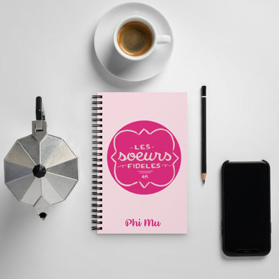 Phi Mu Motto Spiral Notebook in light pink shown with coffee in lifestyle setting