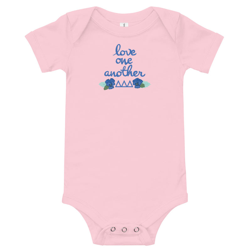 Tri Delta Love One Another Baby Onesie in pink shown flat