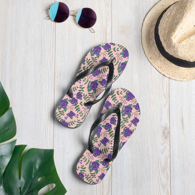 Tri Sigma violet floral print flip flops shown in light pink in lifestyle setting.